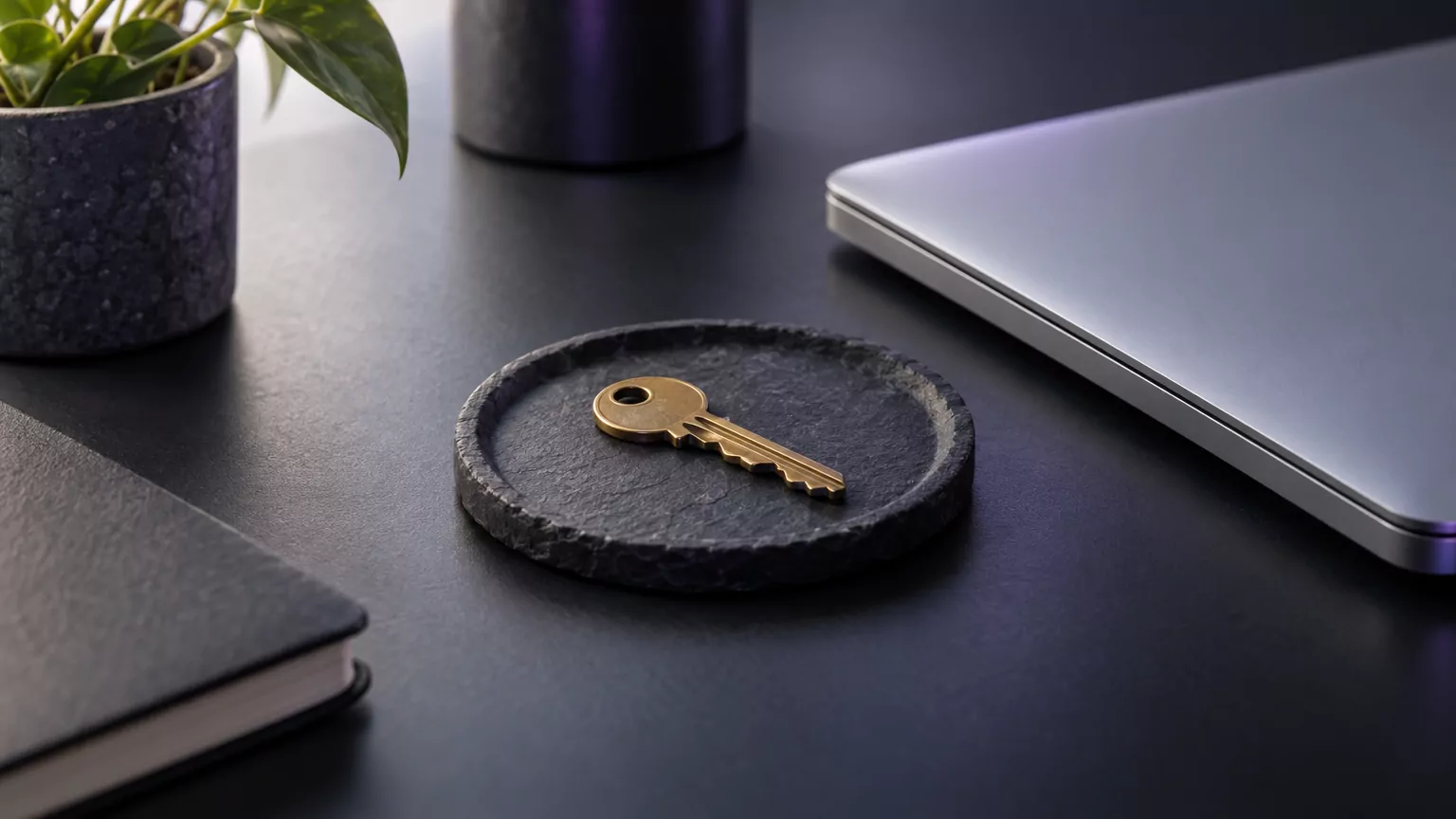 Brass key on a slate tray beside a laptop, standing for the Office licence tied to your Microsoft account